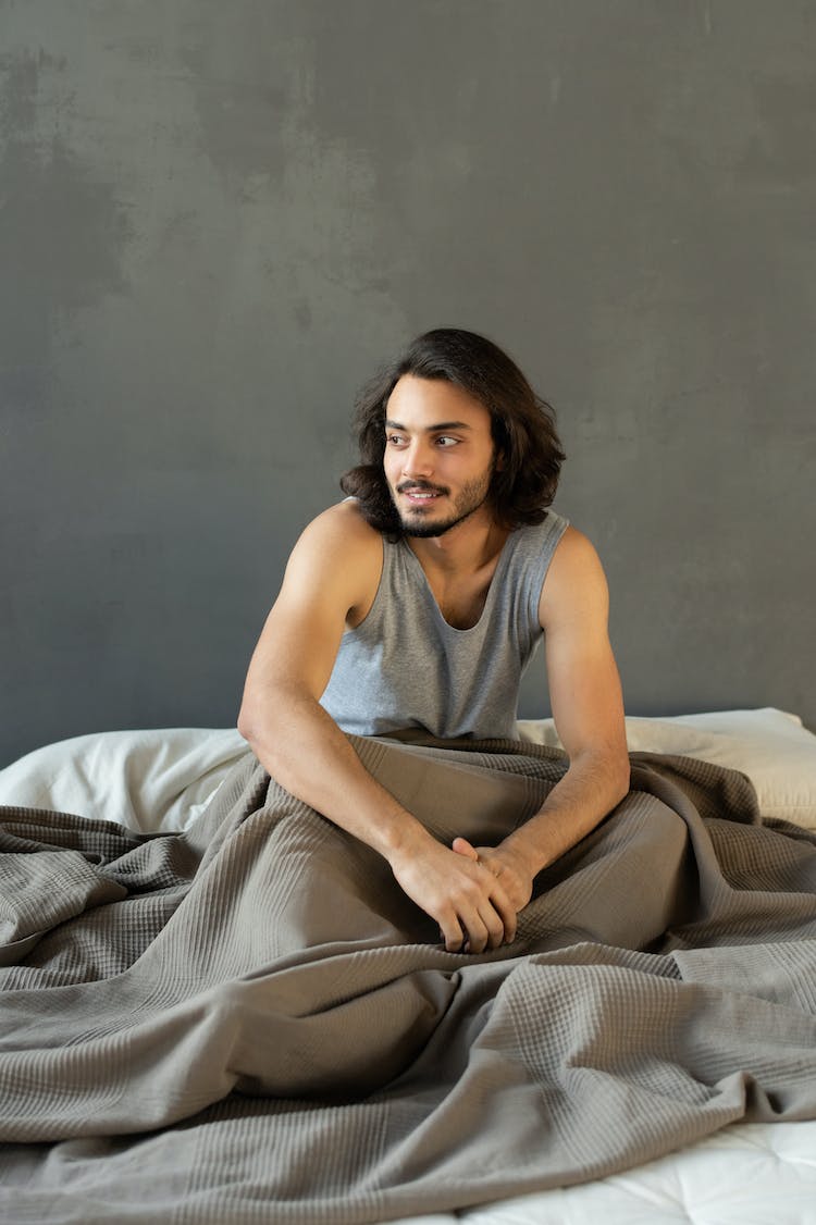 hombre en camiseta gris sin mangas sentado en la cama