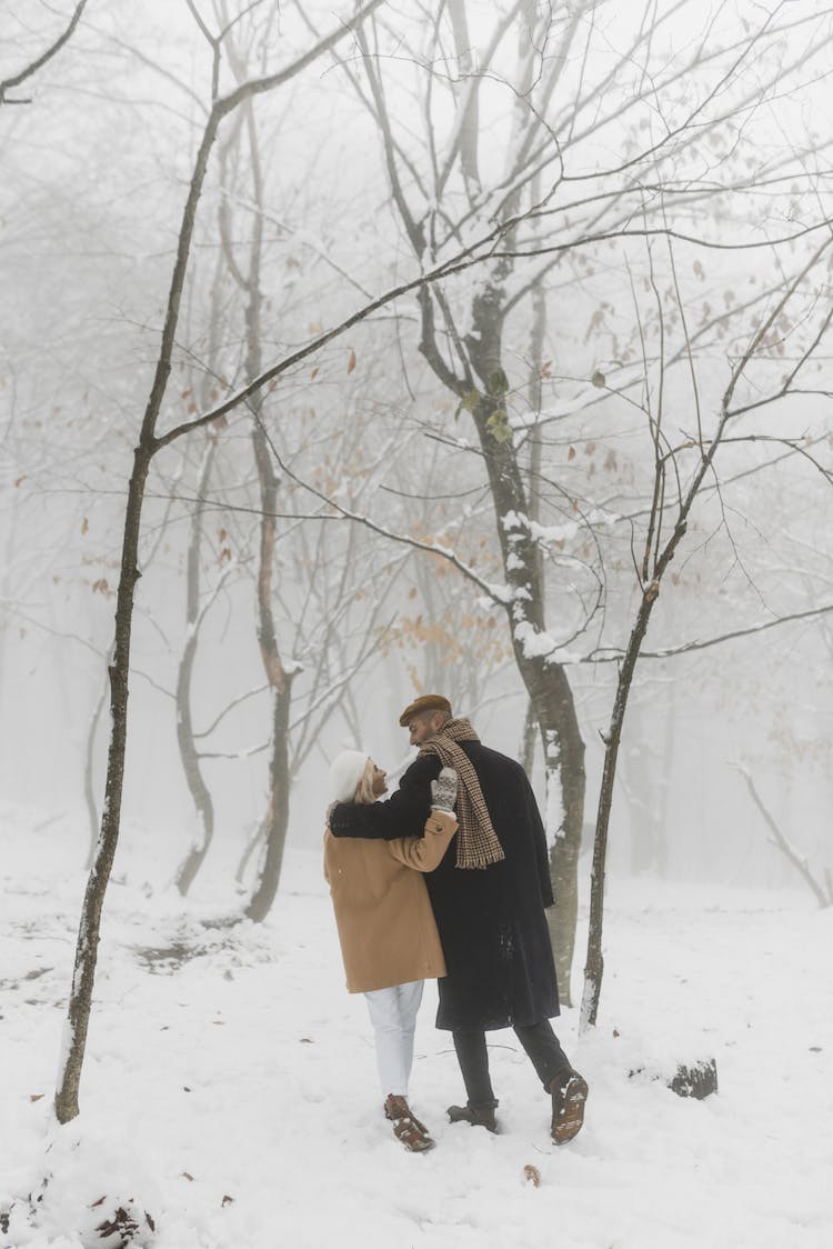 mujer en abrigo negro de pie cerca de un arbol desnudo cubierto de nieve