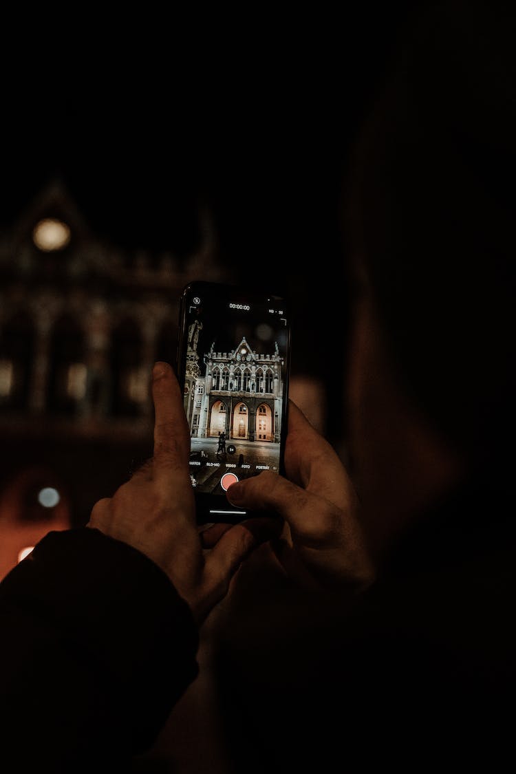 persona sosteniendo smartphone tomando fotos del edificio durante la noche